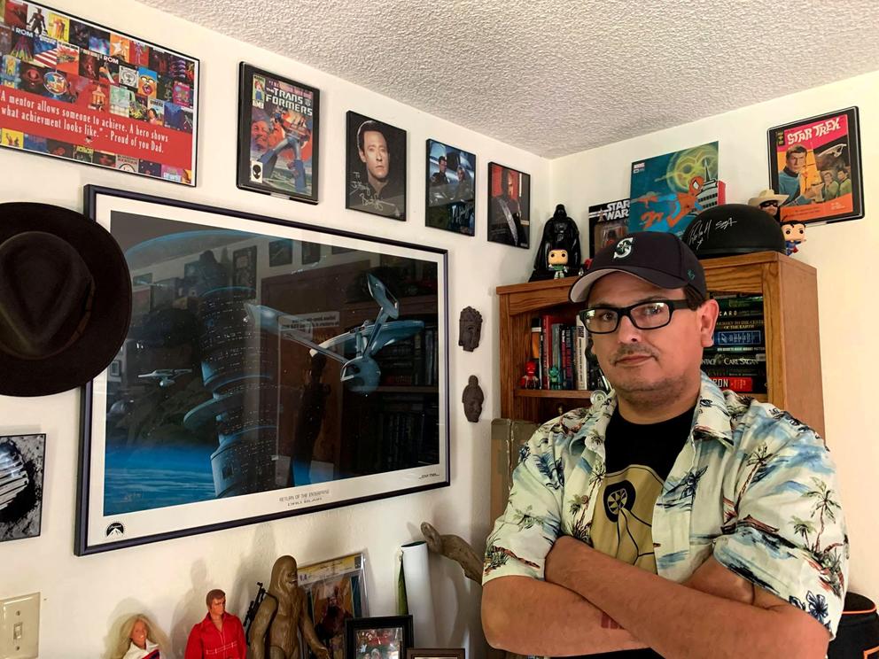 Jeffrey Veregge crosses his arms in front of wall of framed geeky artifacts