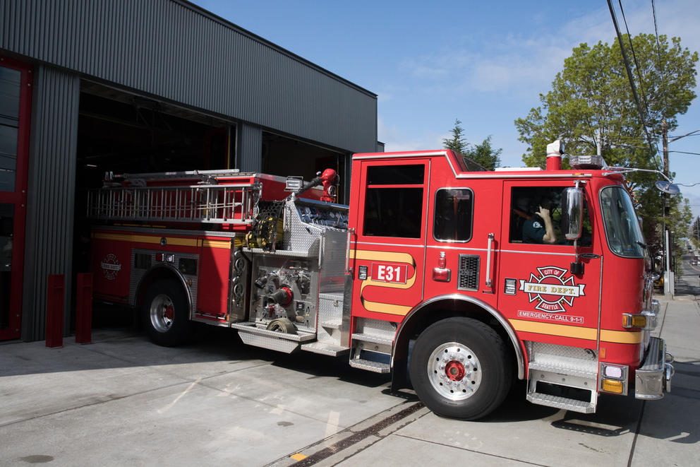 A large fire truck exits a garage beneath a blue sky. 