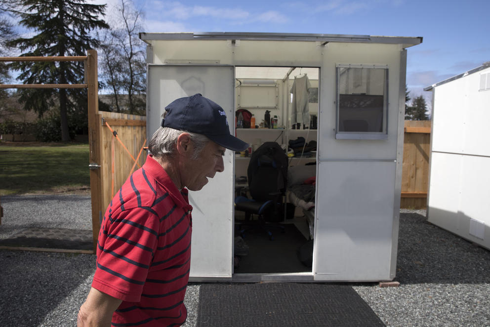 a man walks past a cabin in a tiny home village