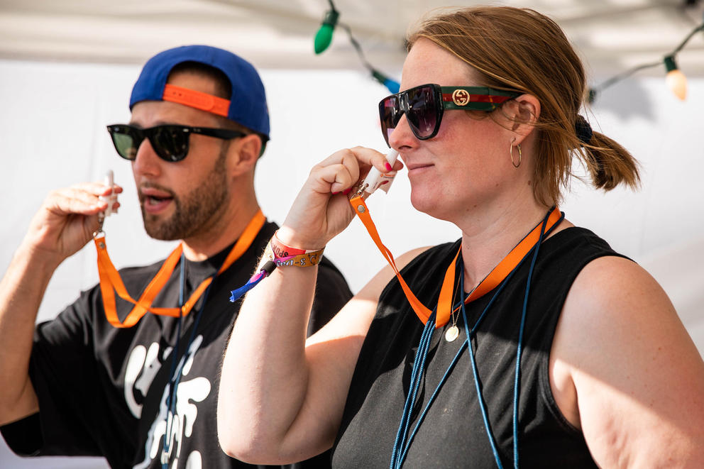 Two people in black t-shirts and sunglasses put a white nasal spray in their nose