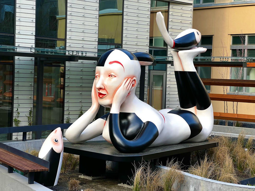 sculpture of a person with black hair and black and white outfit reclining in a fountain