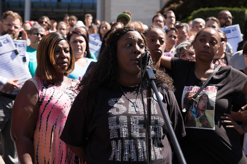 A woman at a microphone with crowd behind