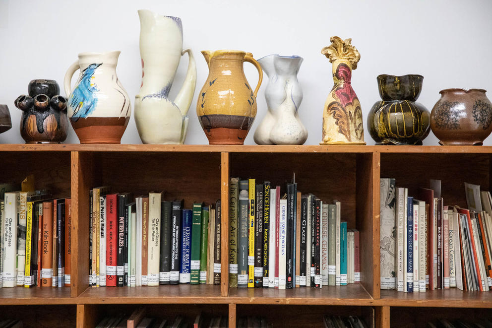 Book case with books and a variety of different vases on top