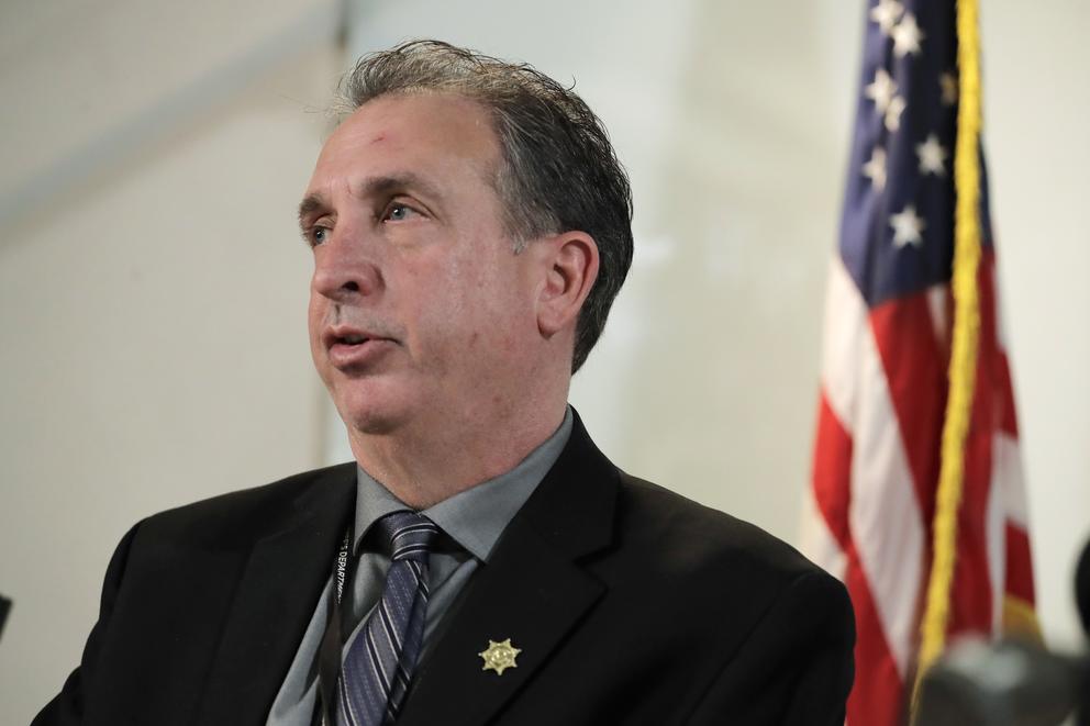 Ed Troyer speaks in suit jacket and tie with an American flag in the background