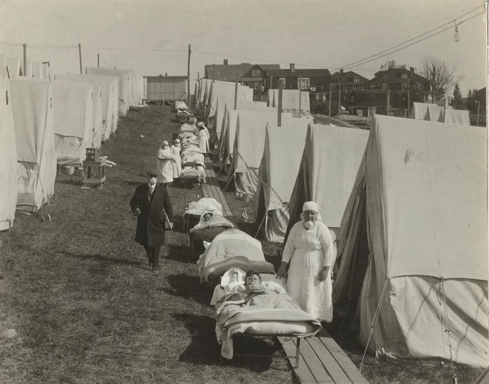 a black and white image of an emergency hospital, with tents and medical personnel as well as patients in beds