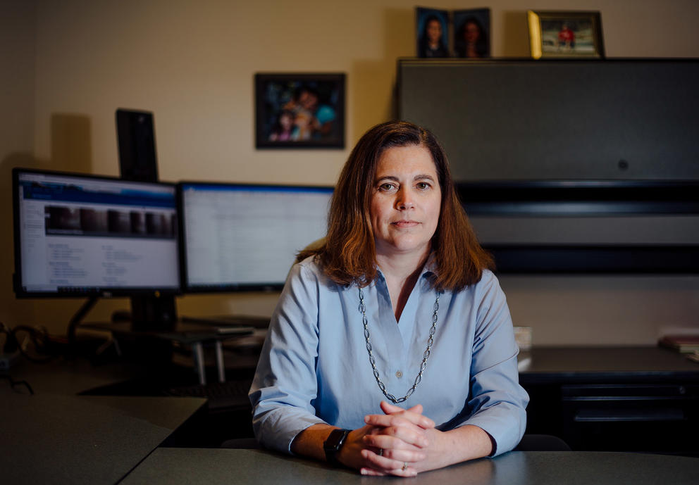 Sadie Armijo sits with her hands crossed on her wooden desk with computer monitors behind her.