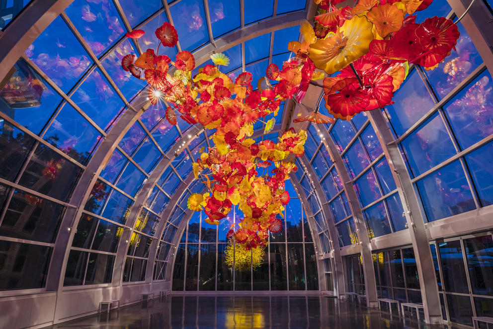 a glass building with a huge orange and red glass sculpture hanging from the ceiling, with the night sky visible behind