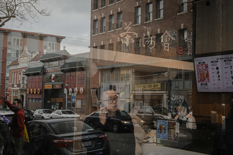 A man on a phone and neighborhood buildings are reflected in a window 