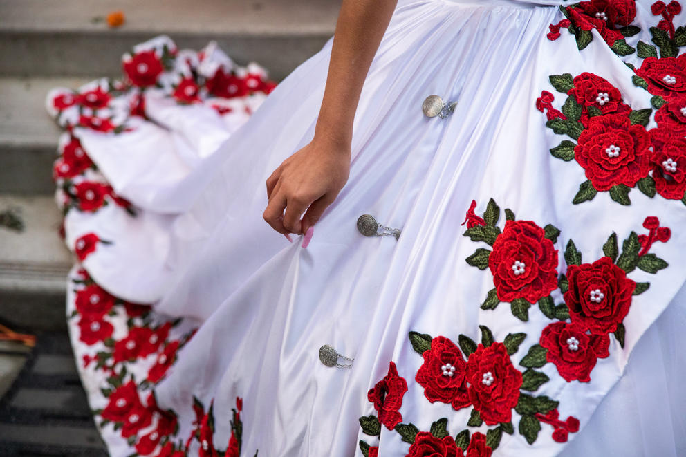 A close up of a hand on a white dress with intricately embroidered red and green flowers
