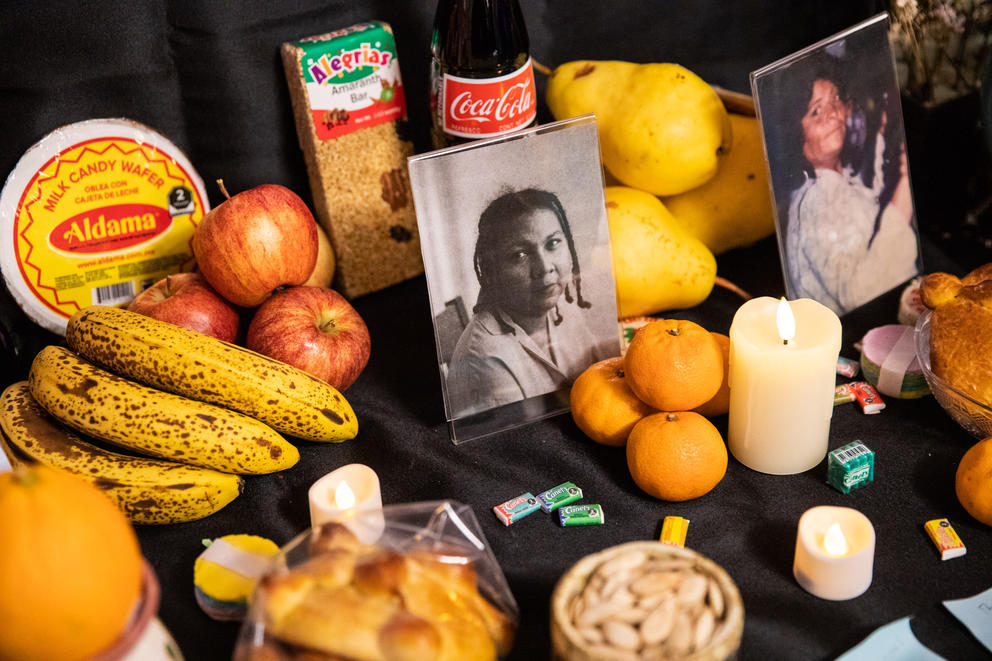 A table with a photo of a woman surrounded by candles, fruit and other food offerings