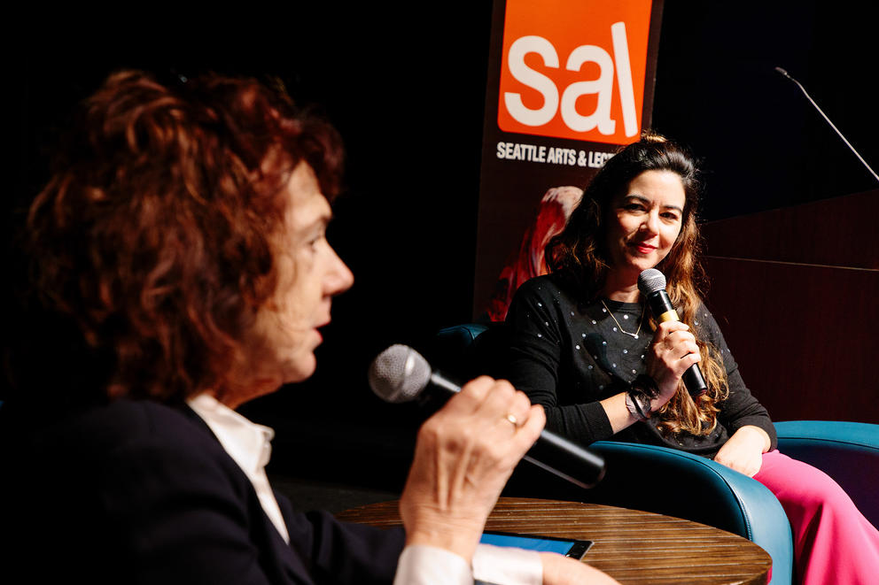 Rebecca Hoogs and Mary Ruefle are seated holding microphones on a stage