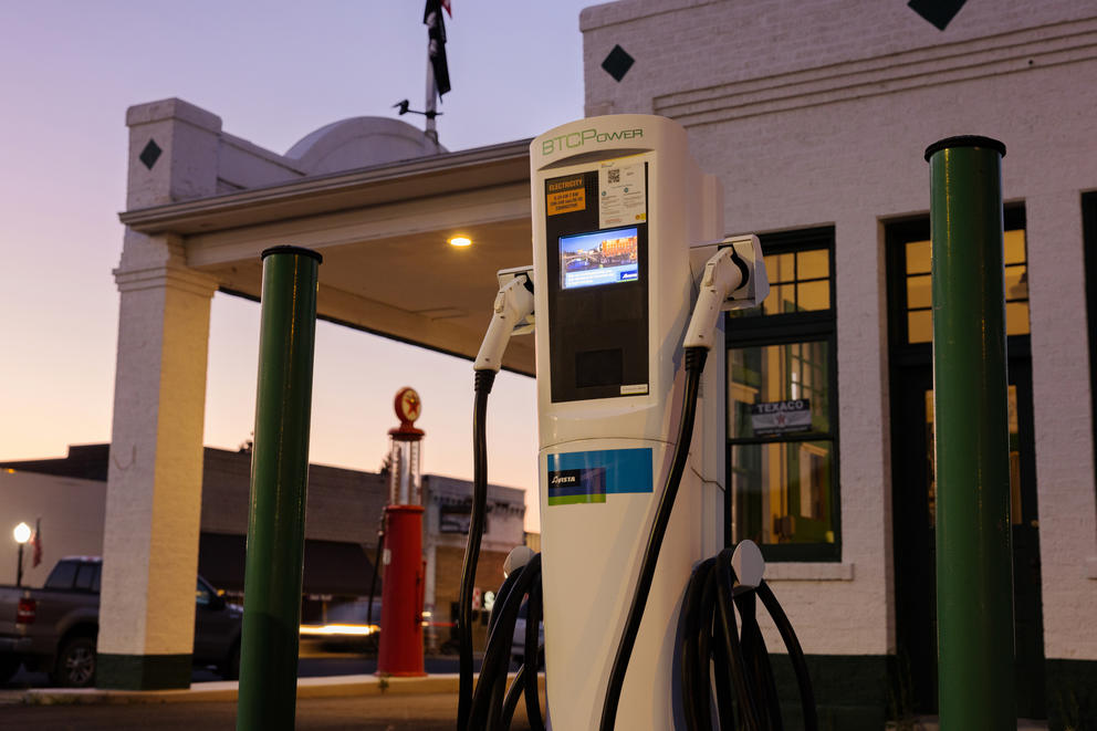 An electric vehicle charger stands near a restored historic gas station. 