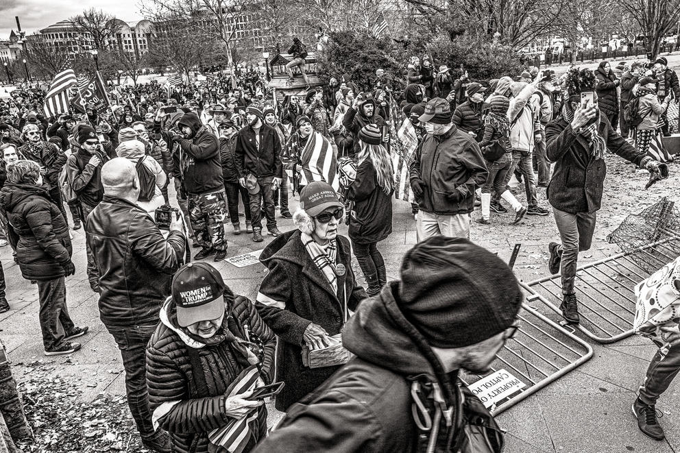 People walk over a fence, one woman wearing earmuffs, another a shopping bag, in a black and white photo