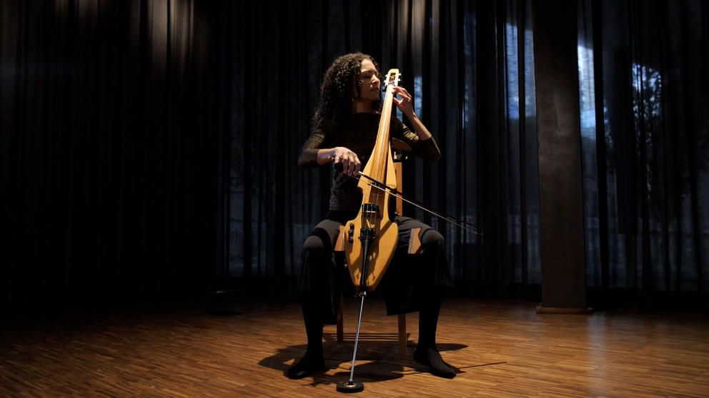 person playing cello with spotlight lighting her and obscuring much of the rest of the room