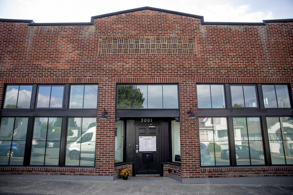 Brick building with six large windows, black door in the middle 