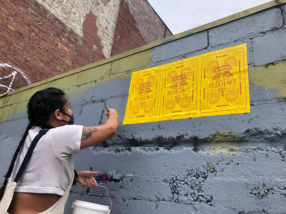 Person in white T-shirt hanging up yellow posters on gray wall