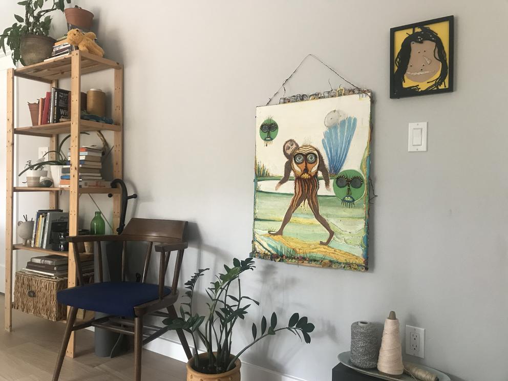 Living room scene with book case and two artworks on wall, plus a plant