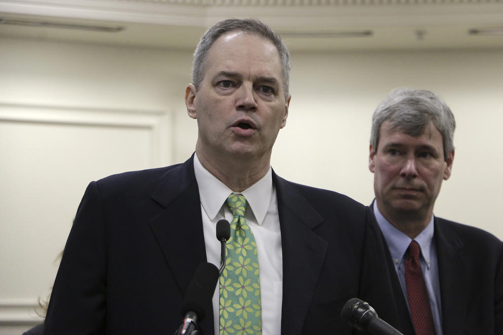 Man in jacket and tie stands in front of microphone