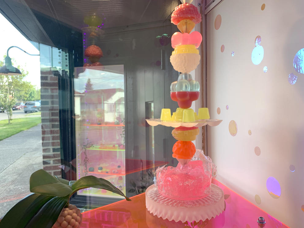 long tower of jelly-like, small sculptures in various pink and yellow colors showcased in a window gallery