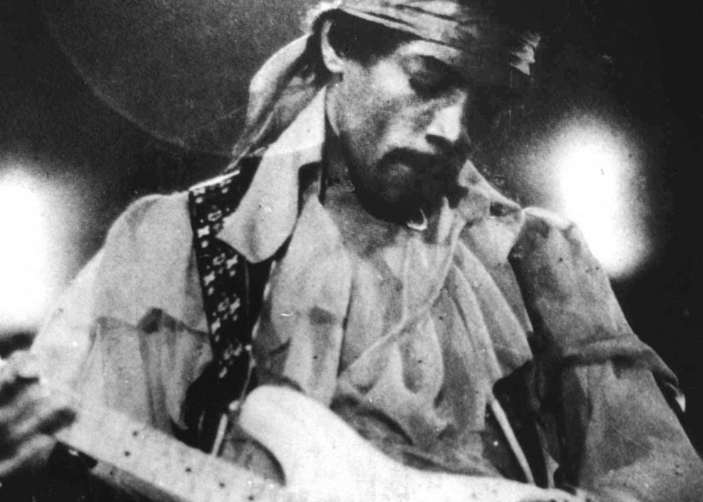 vintage black and white photo of jimi hendrix playing guitar wearing a headband scarf