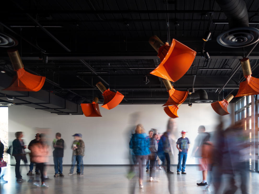 a photo of people in a gallery where large orange speakers hang overhead