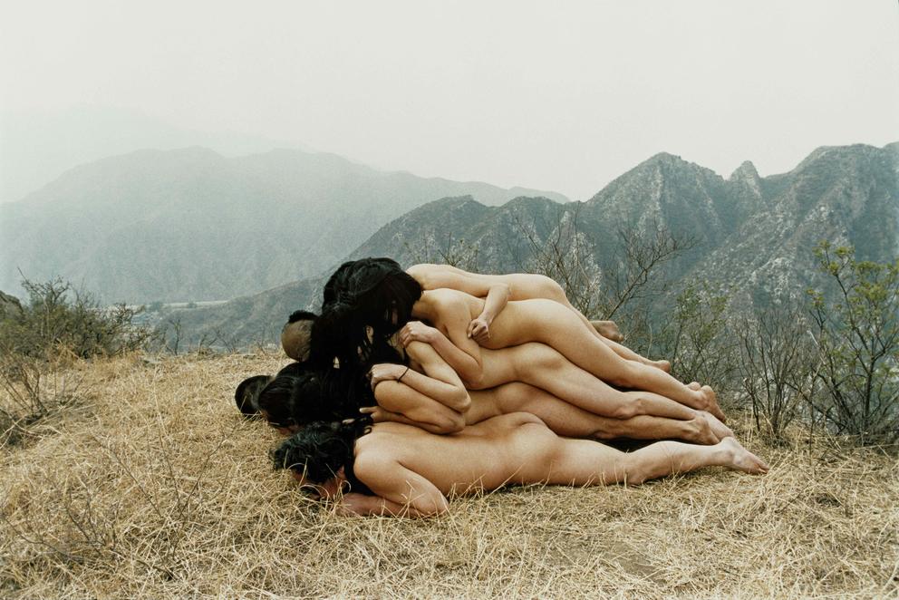 A group of naked people lying stacked on top of each other in nature