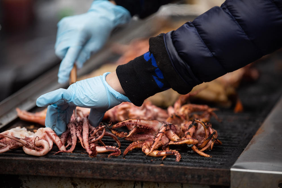 A close up of gloved hands moving squid on a grill