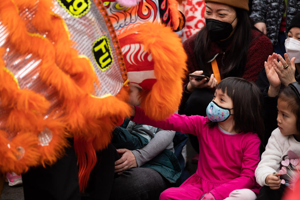 Children reach out to touch the head of an orange Chinese dragon costume