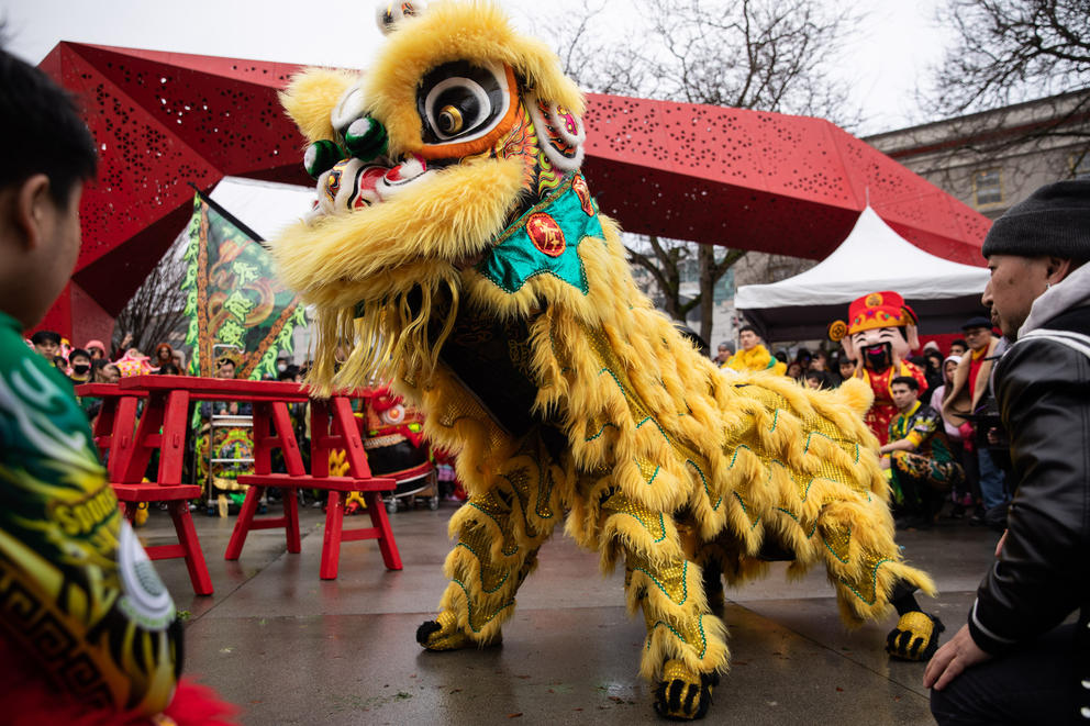 A yellow Chinese lion costume is in a square surrounded by onlookers