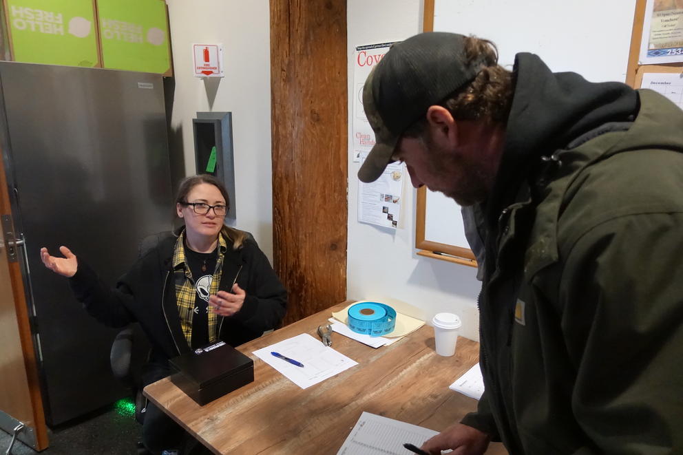 A woman sitting behind a desk talks as a person leans down to fill out an intake form