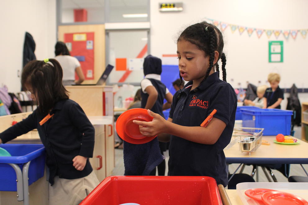 A young girl stands in a classroom holding toy plates