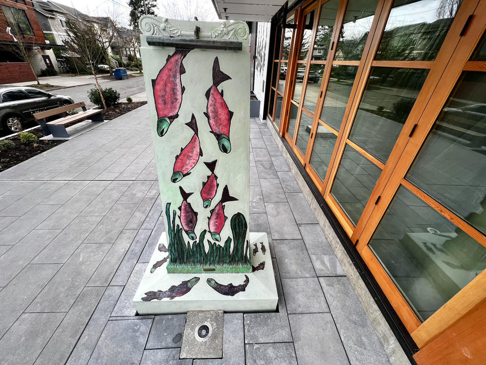 a vertical fountain on a public plaza featuring pink salmon carved into the face