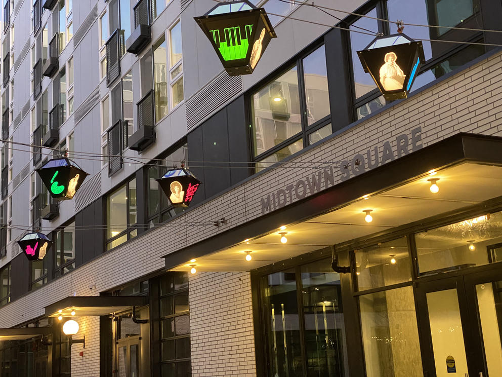 photo of a building entrance with strings of lanterns out front, each embellished with the image of a person and a colorful icon