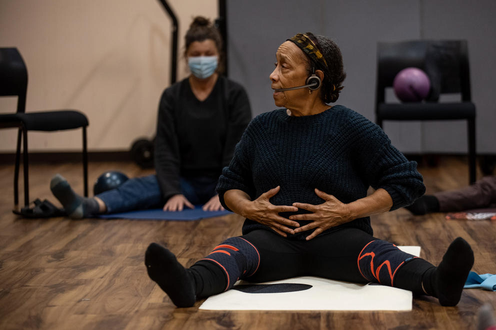 Edna Daigre sits on the floor of a dance studio with her legs outstretched and hands on her stomach