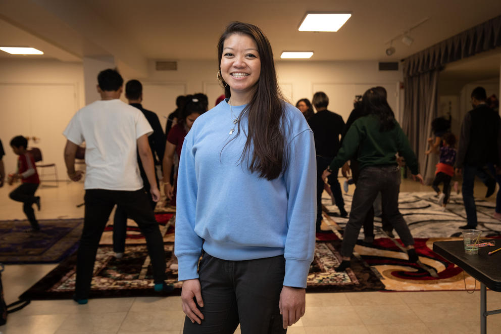 Ung stands for a portrait while community members participate in a dance program behind her.