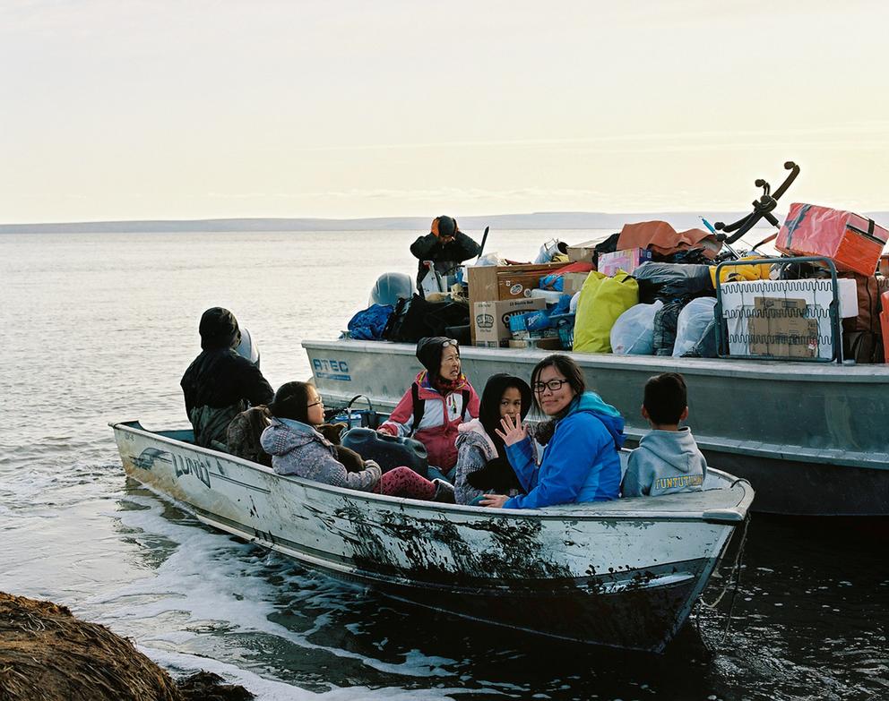 Six people in a small, docked boat. One waves at the camera