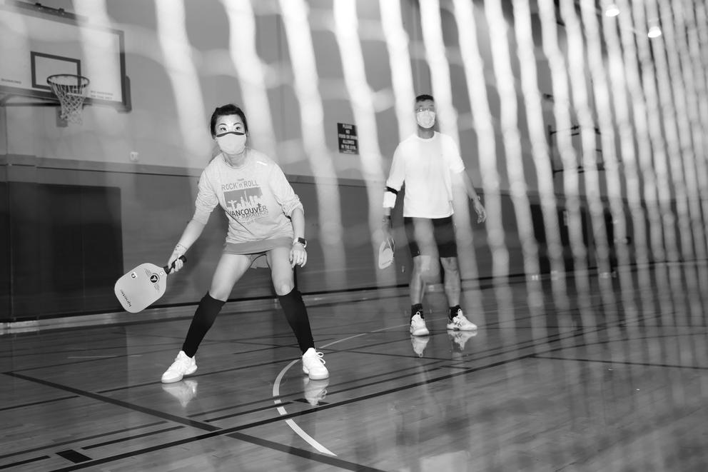 A woman and man are seen playing pickleball through a net. Black and white.