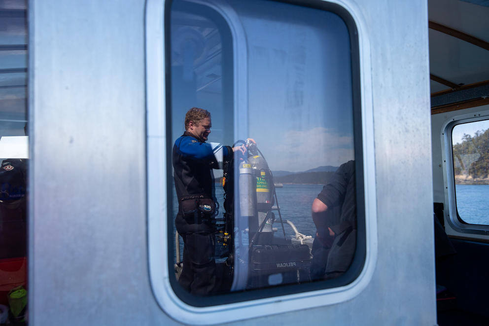 A man in a wetsuit is reflected in a boat window