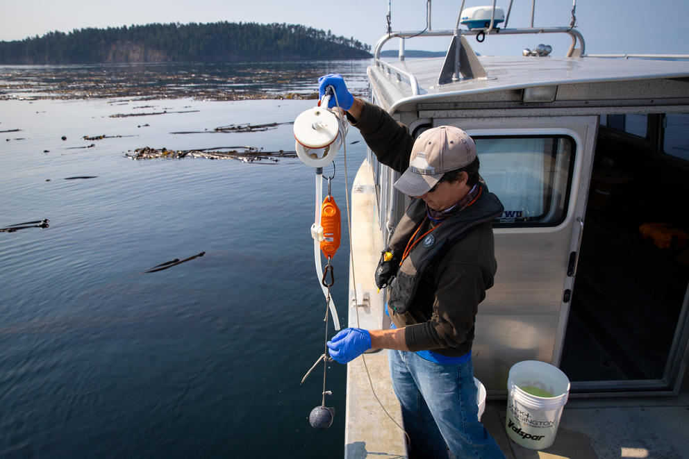 A man holds water sampling equipment off the side of a boat