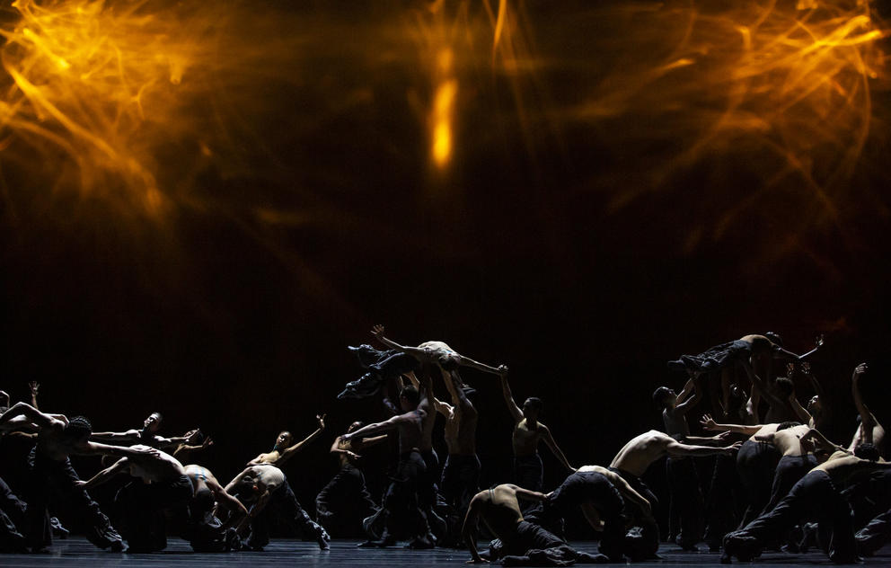 photo of waves of dancers on a dark stage with light bursts above