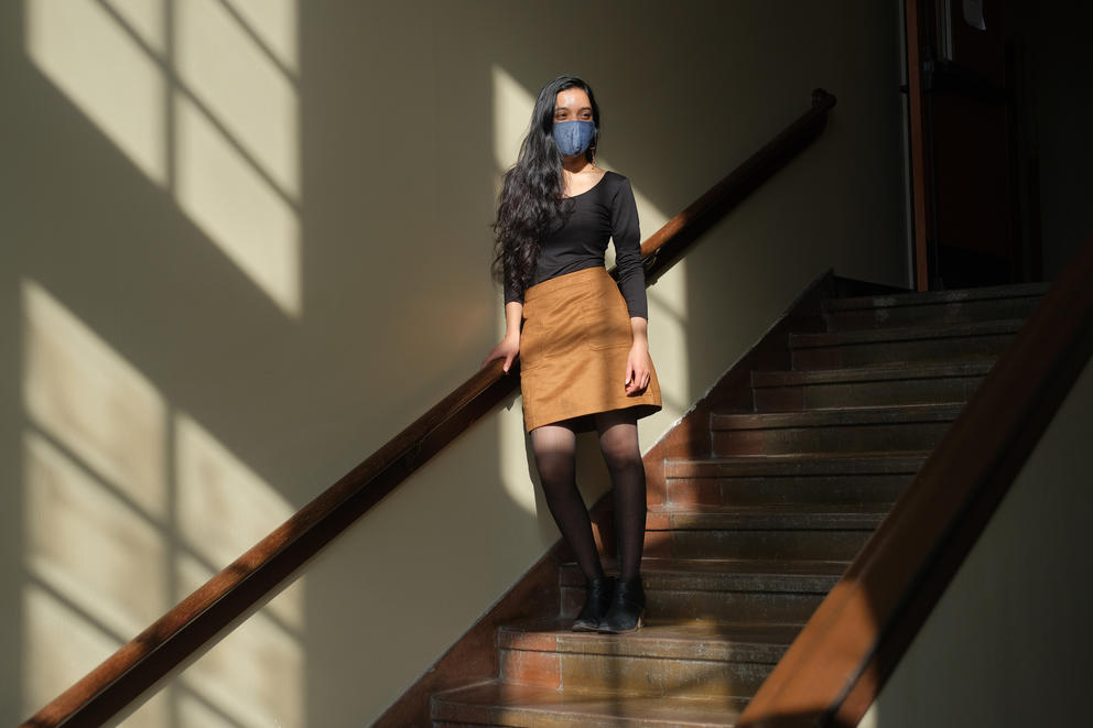 Shraddha Shirude stands in a patch of window light halfway down a set of stairs