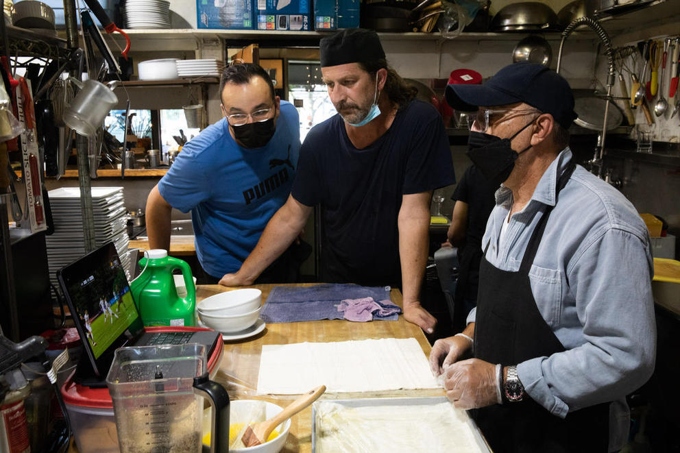 Wali Khairzada,Yama Khairzada, and chef Honza Kirba watch a soccer game together on a laptop in a restaurant kitchen