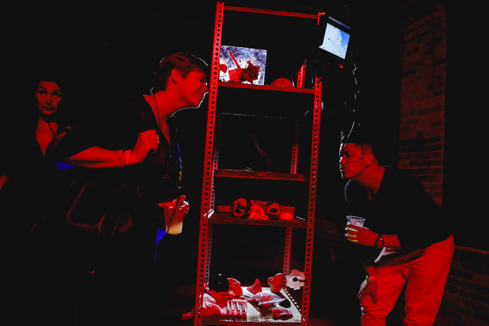 Under red light two people look at a shelf with various sculptures and pieces of art on it