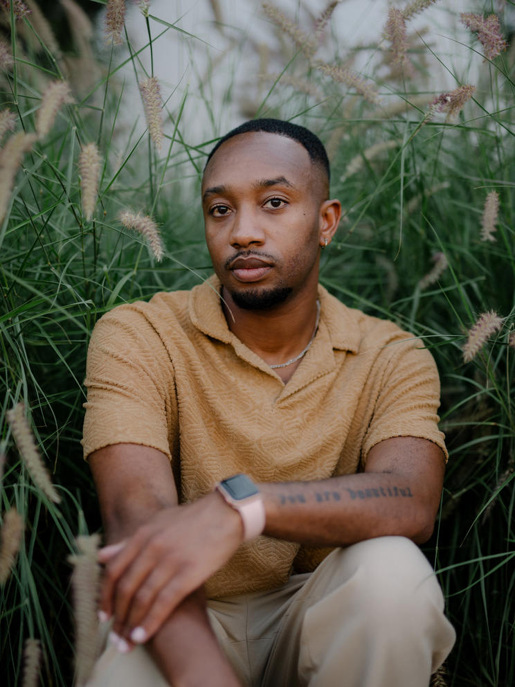 A portrait of Luther Hughes, he is sitting surrounded by willow plants