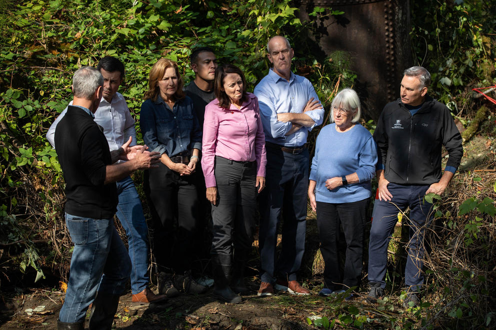 A group of elected officials stands in a group outside surrounded by greenery