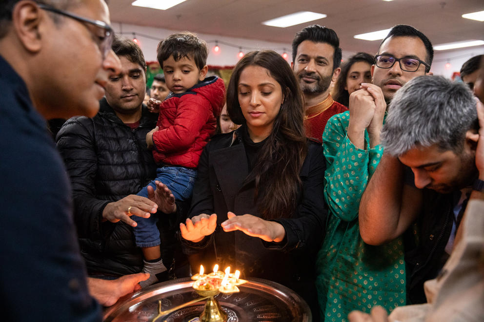 A group of people crowd around a tray with a flame