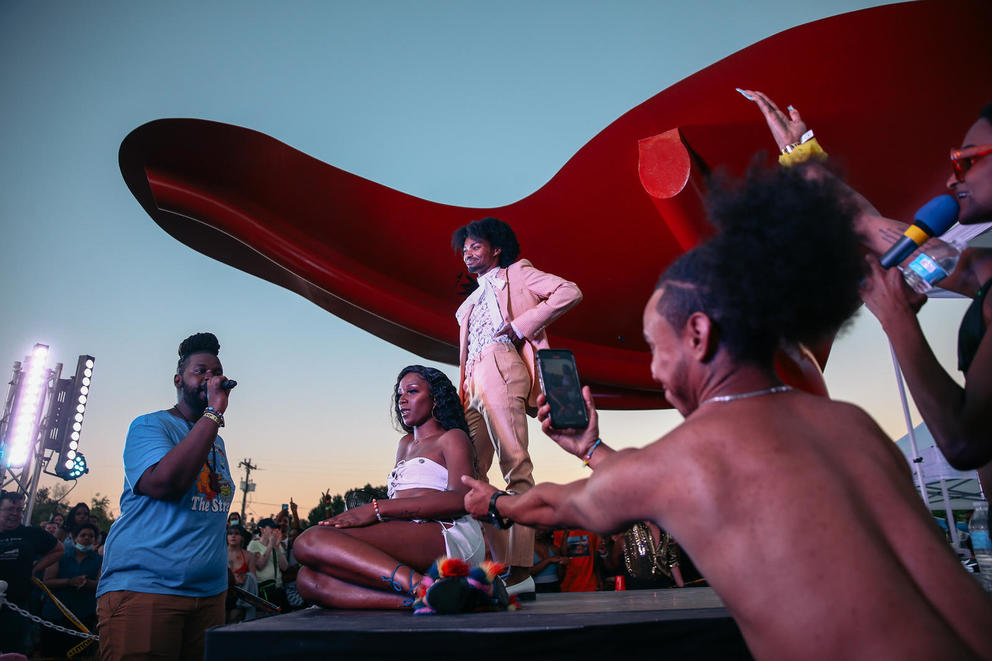 People on a stage sit down and stand up, a red awning above them