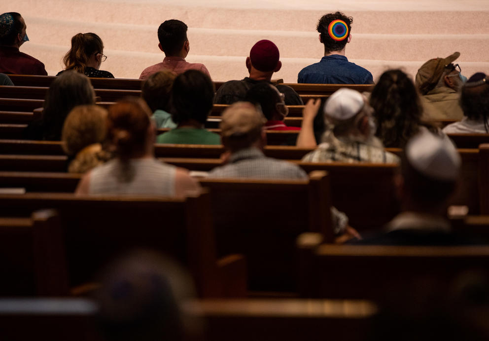 people sit in pews in a synagogue facing away from the camera