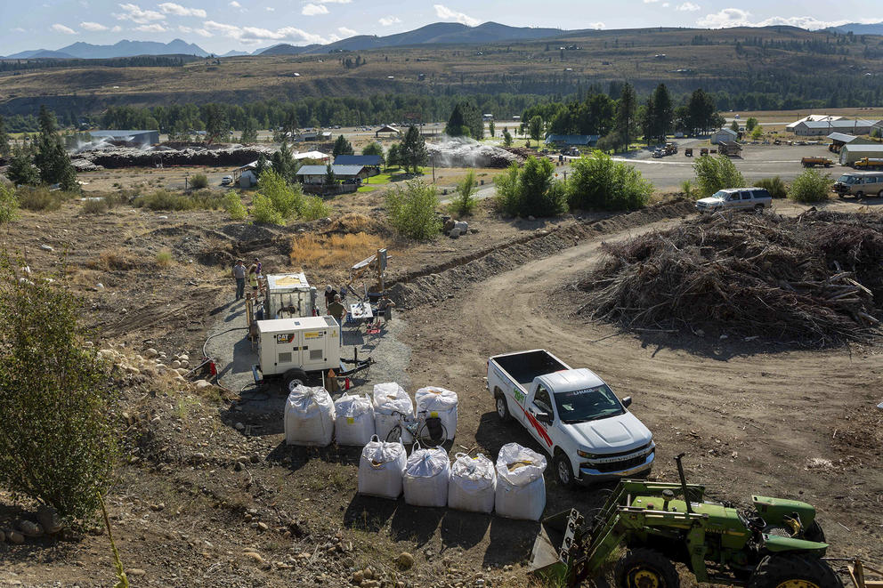 A pile of brush is pictured near a white truck, a generator and a piece of industrial equipment