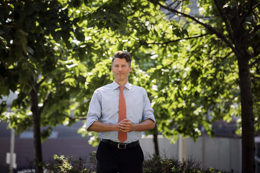 Man in tie stands in front of trees